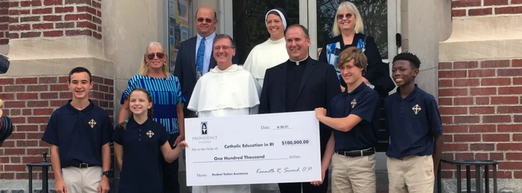 Father Sicard stand in front of a Catholic school with a group of teachers and students